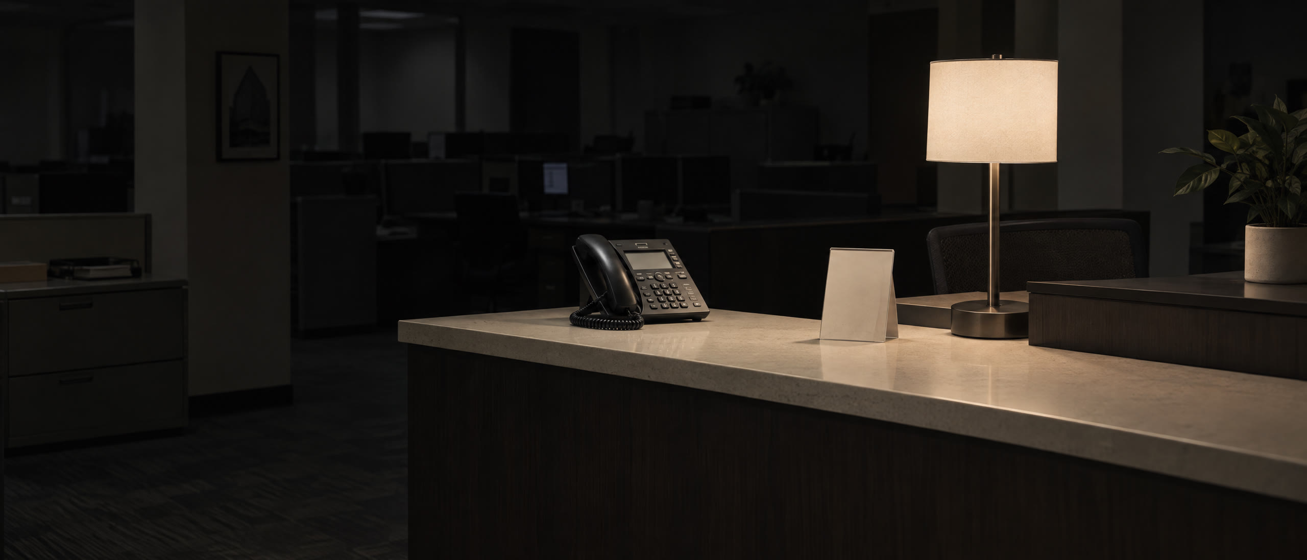 A desk phone and a printed support card on a reception counter at night.